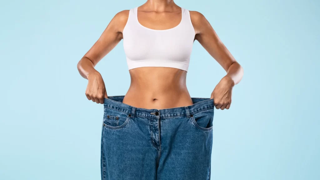 woman holding oversized jeans after weight loss utc ()